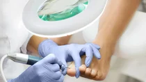 Eine Podologin behandelt mit einem Fußpflegegerät einen Fuß unter einer Lupenlampe.