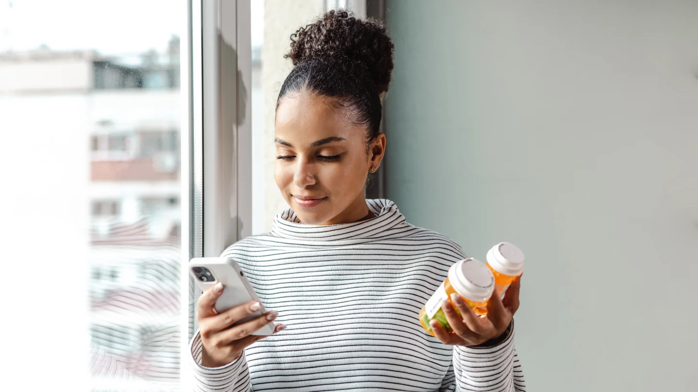 Eine junge Frau hält ein Smartphone und Pillendosen in der Hand. 
