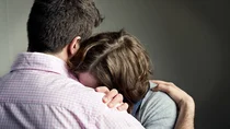 Eine Frau lehnt sich mit dem Kopf an die Schulter eines Mannes. Sie versteckt dabei ihr Gesicht an seiner Brust. Sie wirkt verzweifelt.