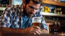 Ein Mann sitzt an einer Bar, h&auml;lt ein Bierglas in der Hand und schaut in den Glas.