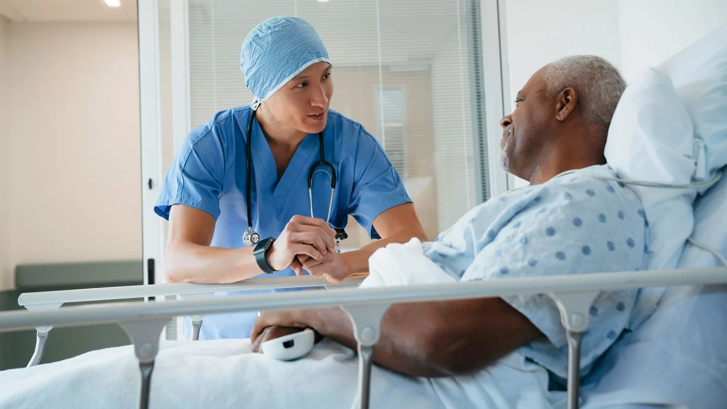 Ein Arzt steht an einem Krankenbett in dem ein Mann aufrecht sitzt.