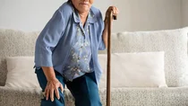 Eine &auml;ltere Dame versucht mit einem Gehstock von einem Sofa auzustehen.