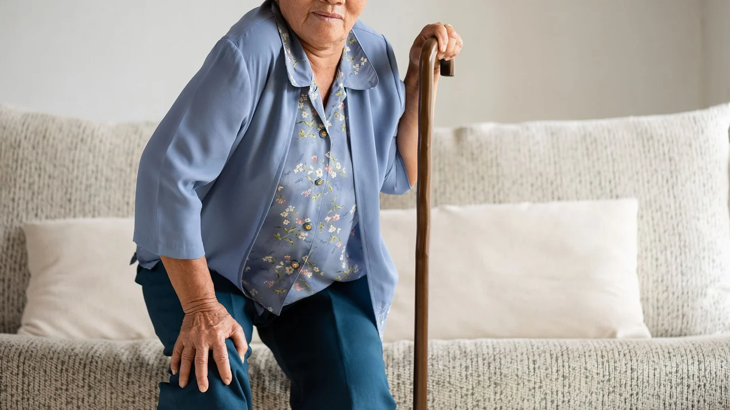 Eine &auml;ltere Dame versucht mit einem Gehstock von einem Sofa auzustehen.