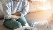 Eine Frau sitzt auf einer Couch, hält ihre Arme verschlossen und presst sie an ihren Bauch. 