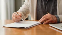 Eine ältere Person sitzt am Tisch und unterschreibt ein Dokument.