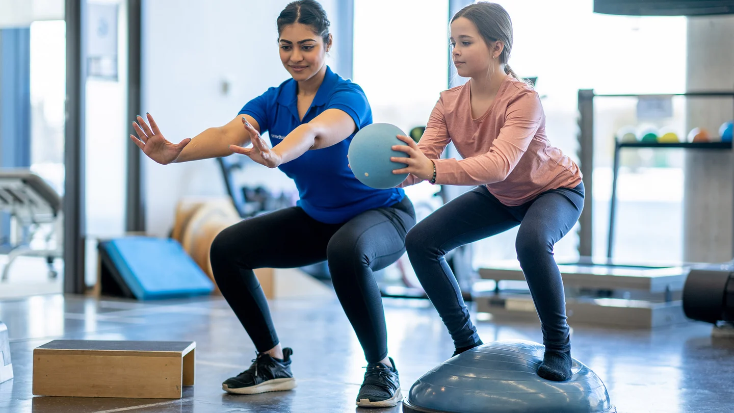 Ein M&auml;dchen macht mit einer Physiotherapeutin &Uuml;bungen mit einem Ball