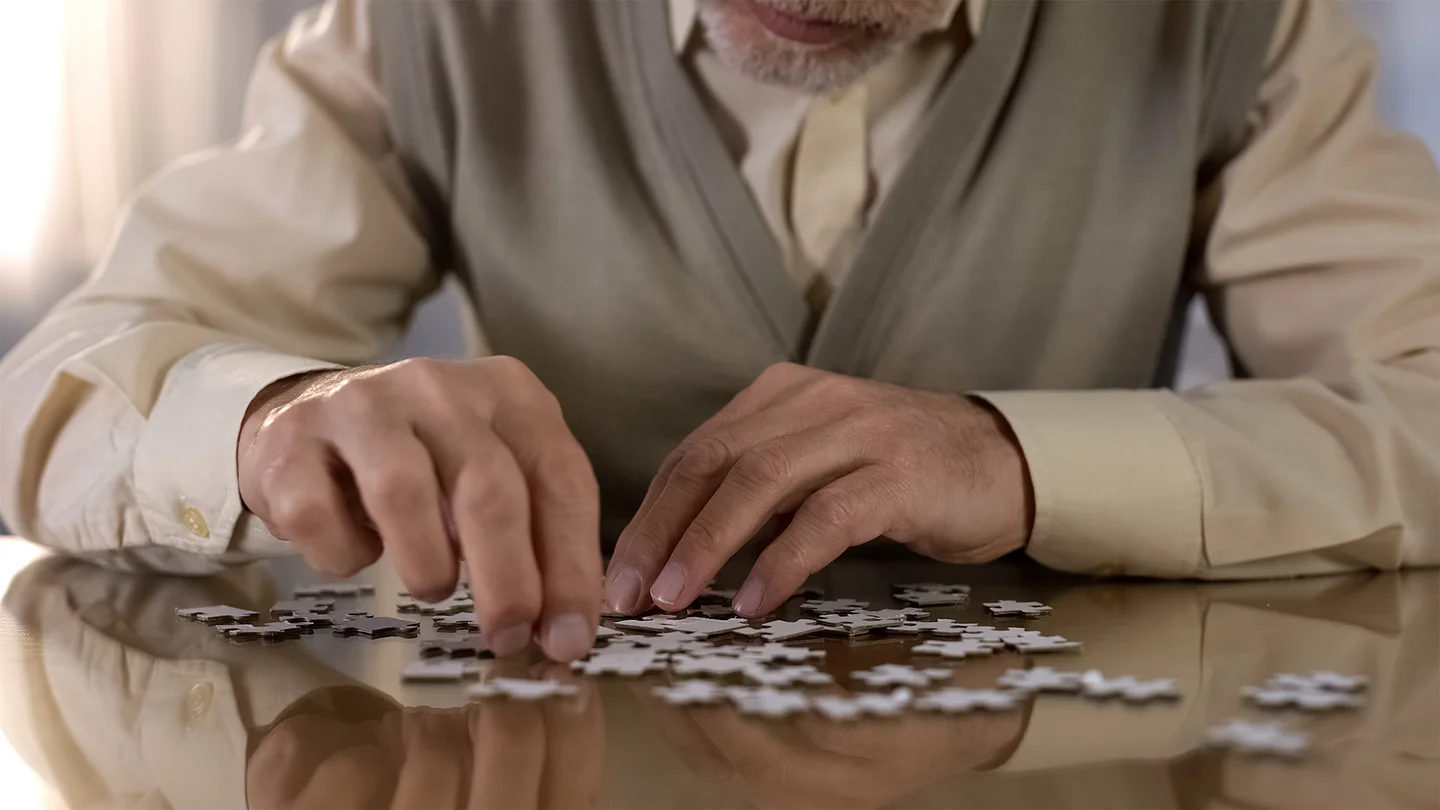 Ein älterer Herr sitzt an einem Tisch und puzzelt.