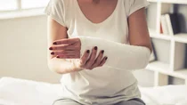 Nahaufnahme einer Frau mit geschientem Unterarm, die auf einer Behandlungsliege sitzt.