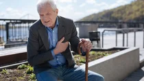 Herzschw&auml;che: Ein &auml;lterer Mann sitzt auf einem Stein und h&auml;lt sich mit einer Hand sein Herz. Sein Gesicht ist angespannt und schmerzverzerrt.