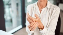 Eine Frau fasst sich an die schmerzende linke Hand.