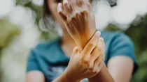 Karpaltunnelsyndrom: Eine Frau hält ihre Arme in die Luft und fasst sich ans linke Handgelenk.