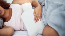Eine Frau liegt im Bett mit Wärmflasche auf dem Bauch.