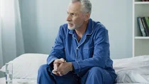 Mann mittleren Alters sitzt nachdenklich auf einem Bett 
