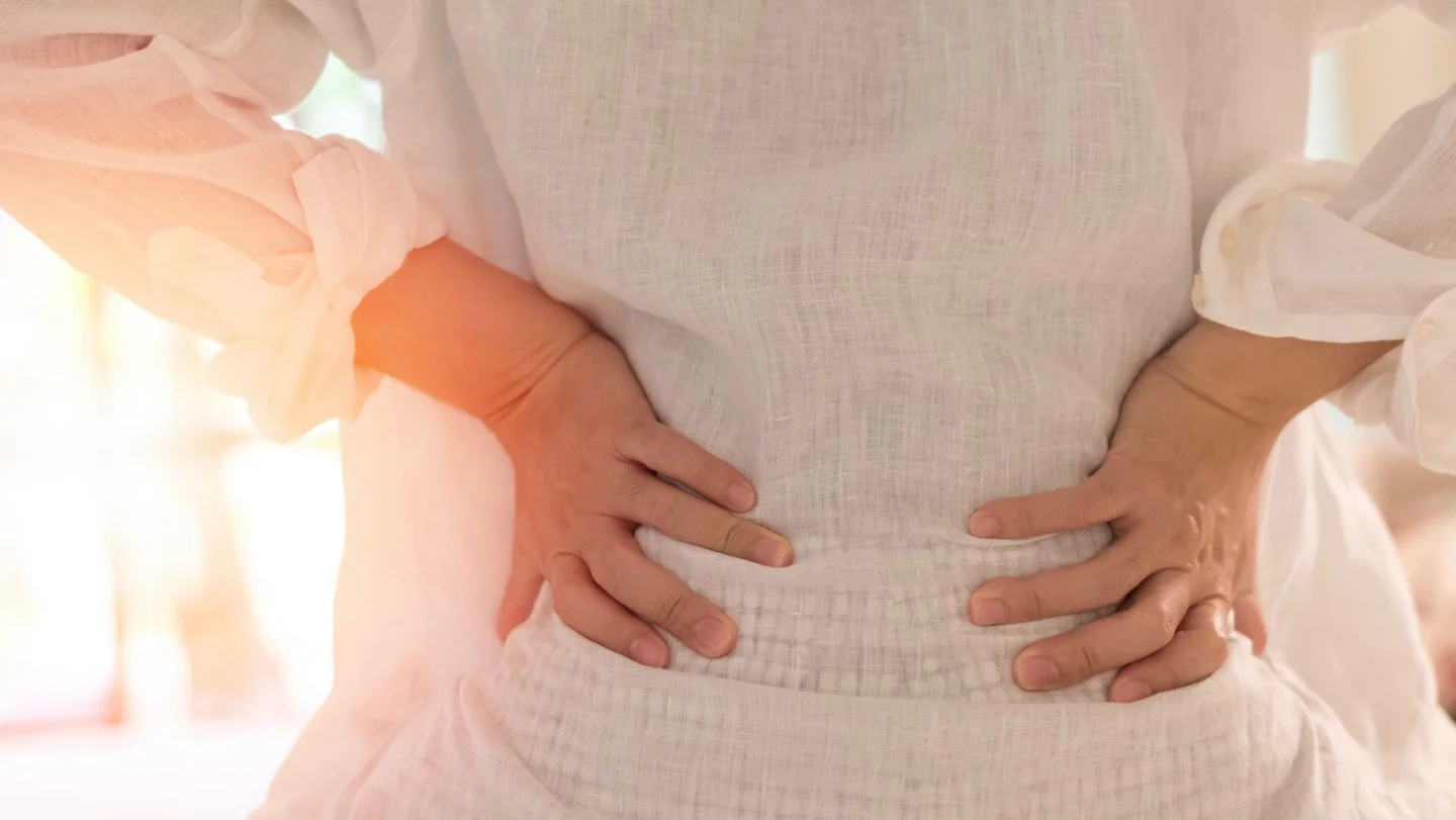 Eine Frau legt beide Hände an ihre Taille und beugt leicht ihren Oberkörper nach hinten.