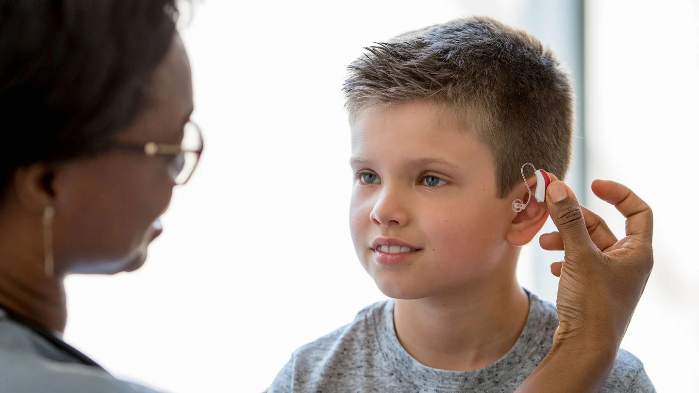 Eine Frau legt einem kleinen Jungen ein Hörgerät an.