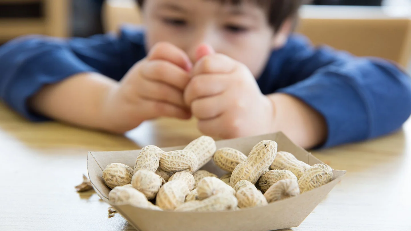 Nahrungsmittelallergie: Ein Junge sitzt an einem Tisch vor einer Schale mit Erdn&uuml;ssen.