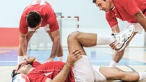 Ein Fußballer liegt verletzt auf dem Boden einer Sporthalle. 