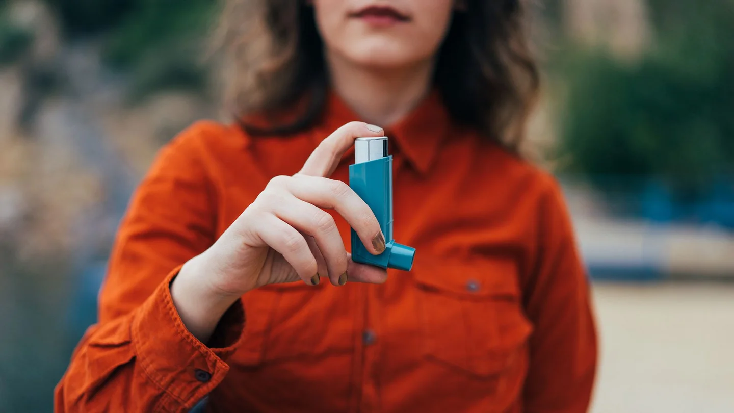 Eine Frau hält ein Asthmaspray in der Hand.