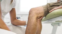 Eine Ärztin untersucht die Kniekehle eines Patienten.