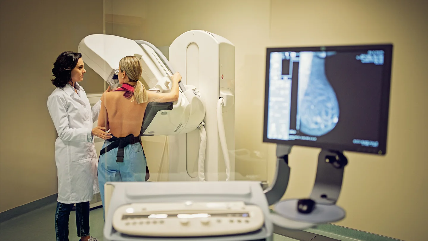 Krebsfr&uuml;herkennung: Eine Patientin bekommt ein Mammografie-Screening. Neben der Frau steht eine &Auml;rztin. Sie f&uuml;hrt die Untersuchung durch. Auf einem Bildschirm ist das R&ouml;ntgenbild der Brust zu sehen.