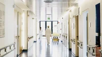 Krankenhauspersonal in weißer Arbeitskleidung läuft durch einen hellen Krankenhausflur.