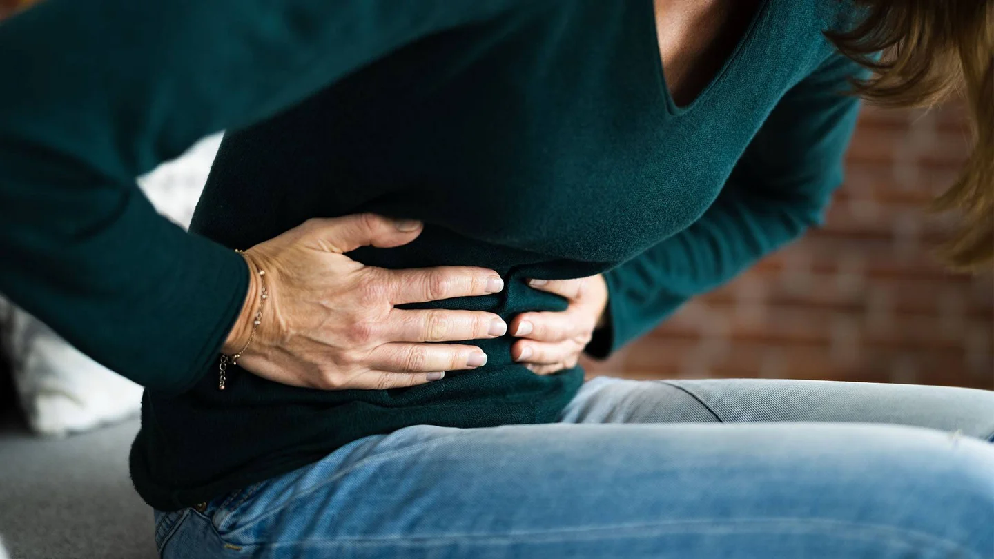 Eine Frau fasst sich mit beiden Händen auf die Bauchdecke.