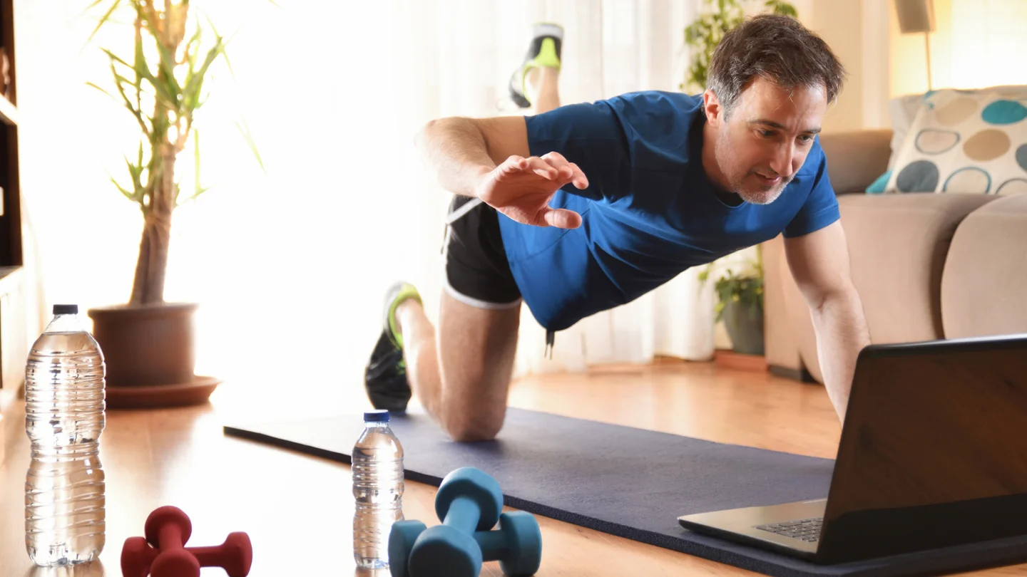 Ein Mann macht auf der Yogamatte Übungen vor seinem Laptop.