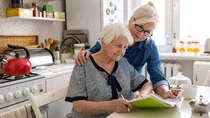 Eine Frau hilft einer Seniorin bei dem Ausfüllen eines Dokumentes