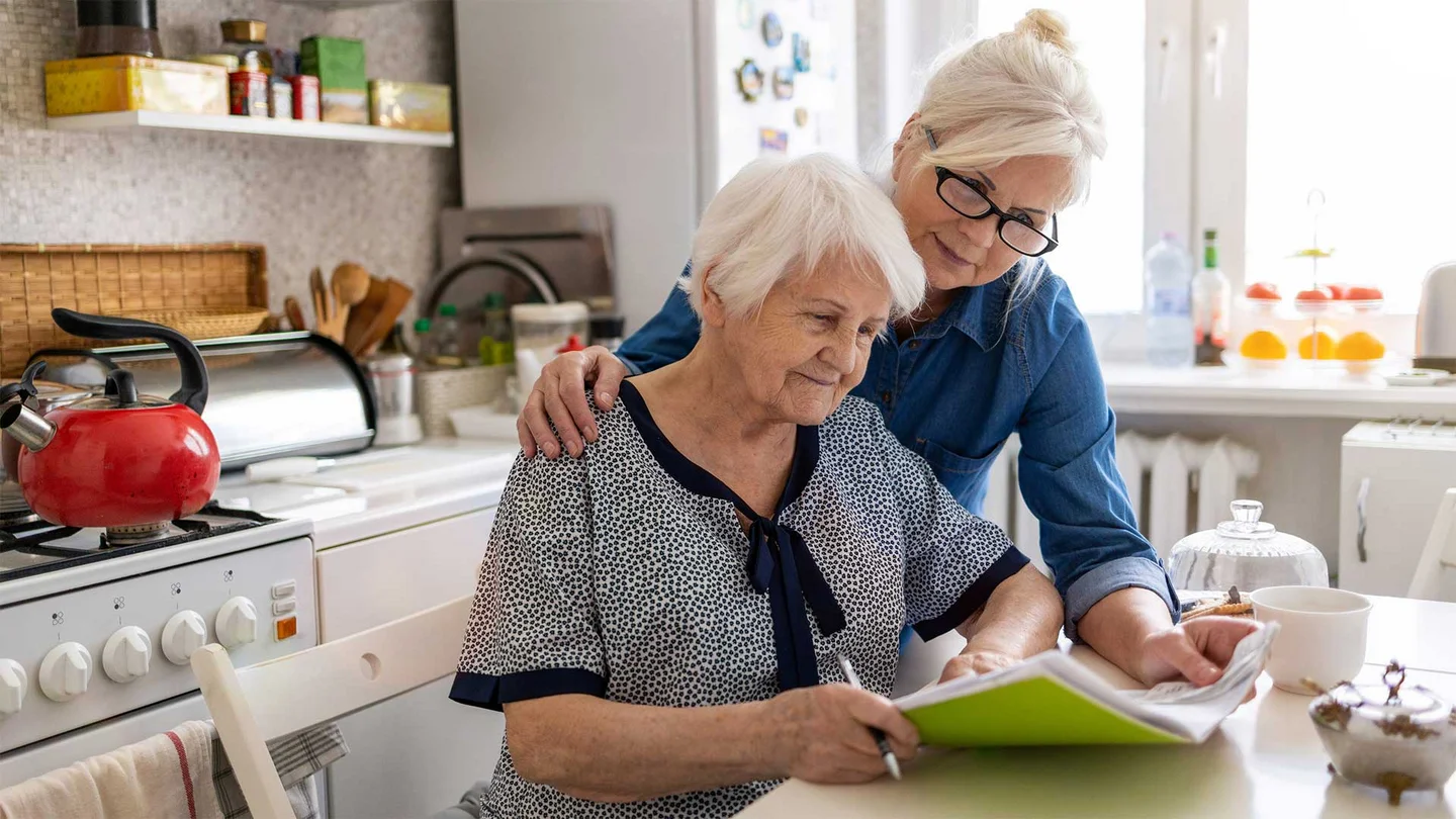 Eine Frau hilft einer Seniorin bei dem Ausfüllen eines Dokumentes