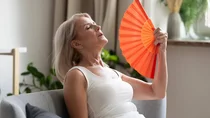 Eine Frau im Top lehnt sich ersch&ouml;pft zur&uuml;ck und f&auml;chert sich mit einem F&auml;cher Luft zu.