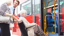 Ein junger Busfahrer schiebt einen &auml;lteren Herrn im Rollstuhl &uuml;ber eine Rampe in den Bus.