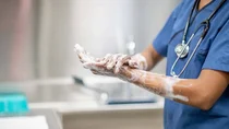 Medizinische Fachkraft in blauer OP-Kleidung w&auml;scht sich H&auml;nde und Unterarme mit Desinfektionsseife