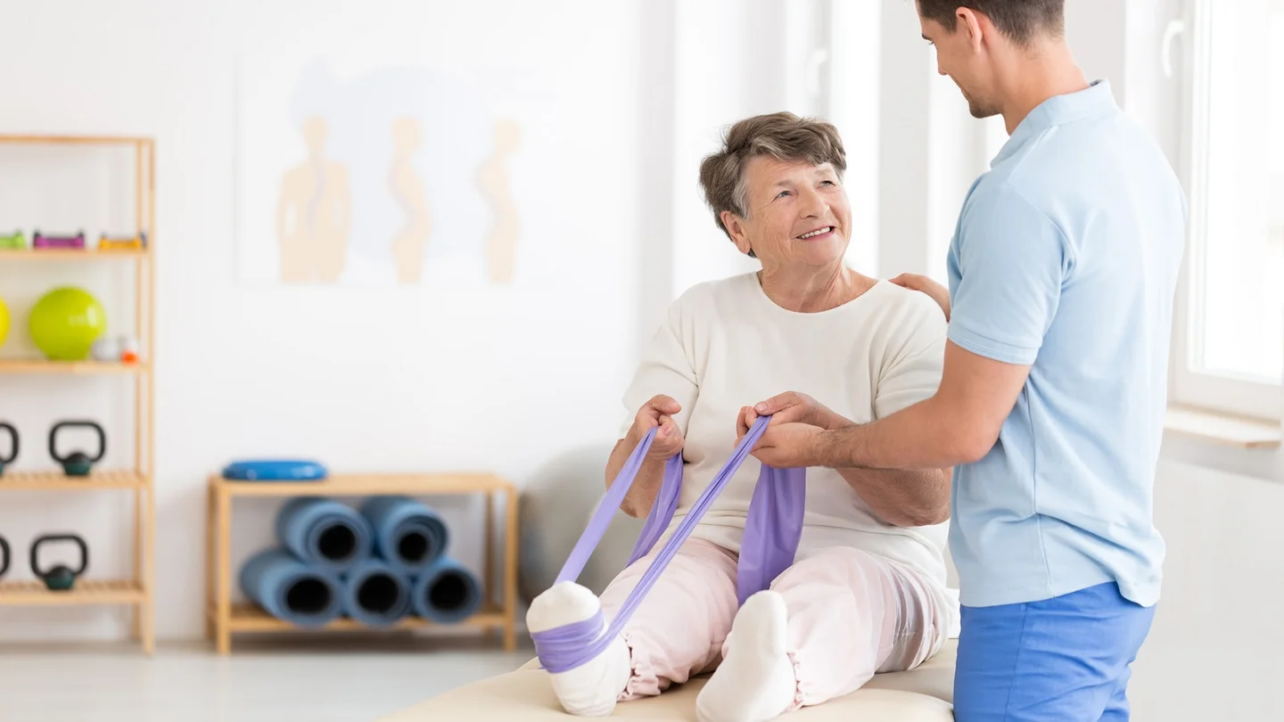 Eine &auml;ltere Frau trainiert unter Anleitung mit einem Fitnessband
