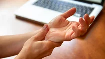Eine Frau fasst sich ans Handgelenk und presst ihren Daumen auf die Handwurzel.