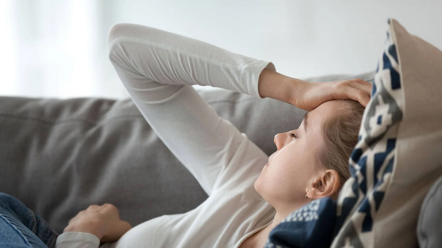 Eine junge Frau liegt erschöpft auf der Couch. 