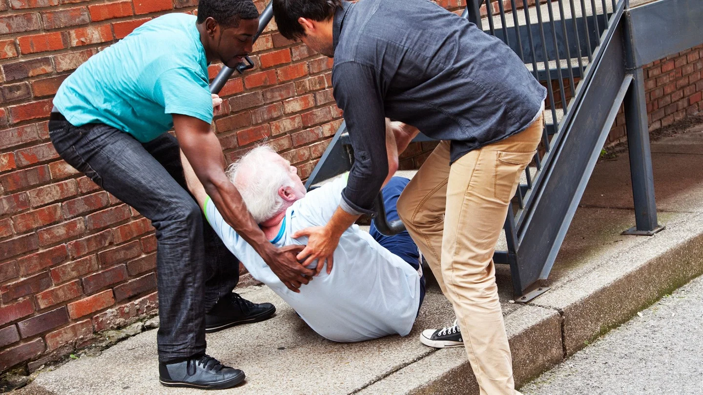 Ein Senior ist auf der Treppe gestürzt. Zwei Männer helfen ihm auf.