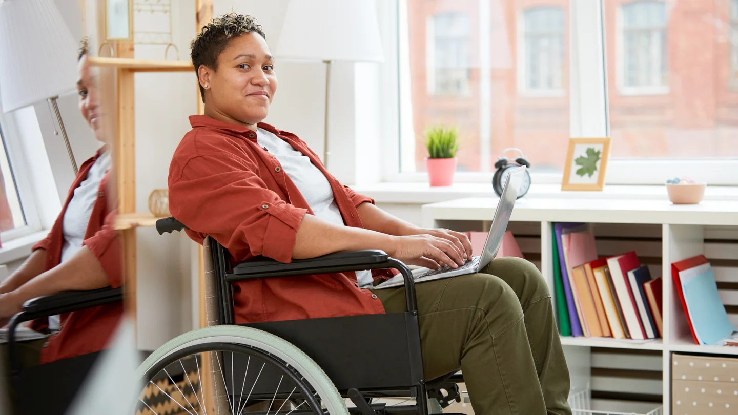 Frau sitzt im Rollstuhl mit Laptop auf dem Scho&szlig;.
