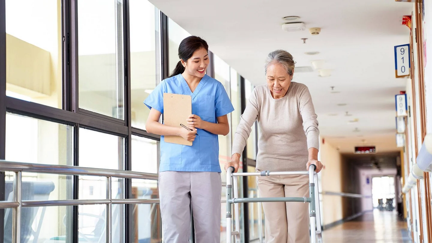 Eine Pflegerin begleitet eine Seniorin mit Gehhilfe.