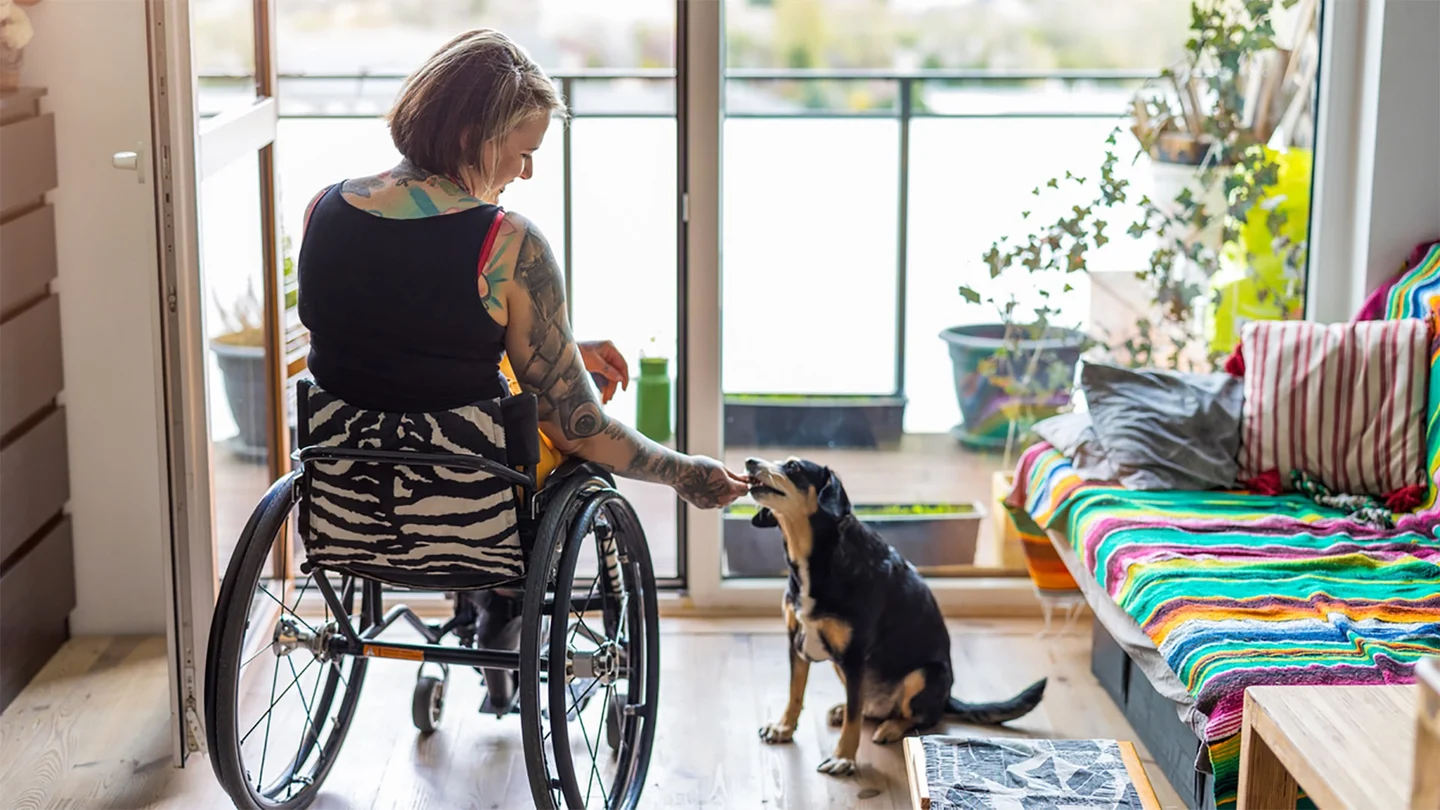Eine Frau im Rollstuhl füttert einen Hund.