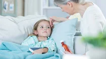 Kleines Mädchen liegt krank auf dem Sofa, die Großmutter pflegt es.