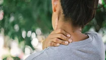 Nackenschmerzen: Eine Frau massiert sich ihren Nacken mit der linken Hand.