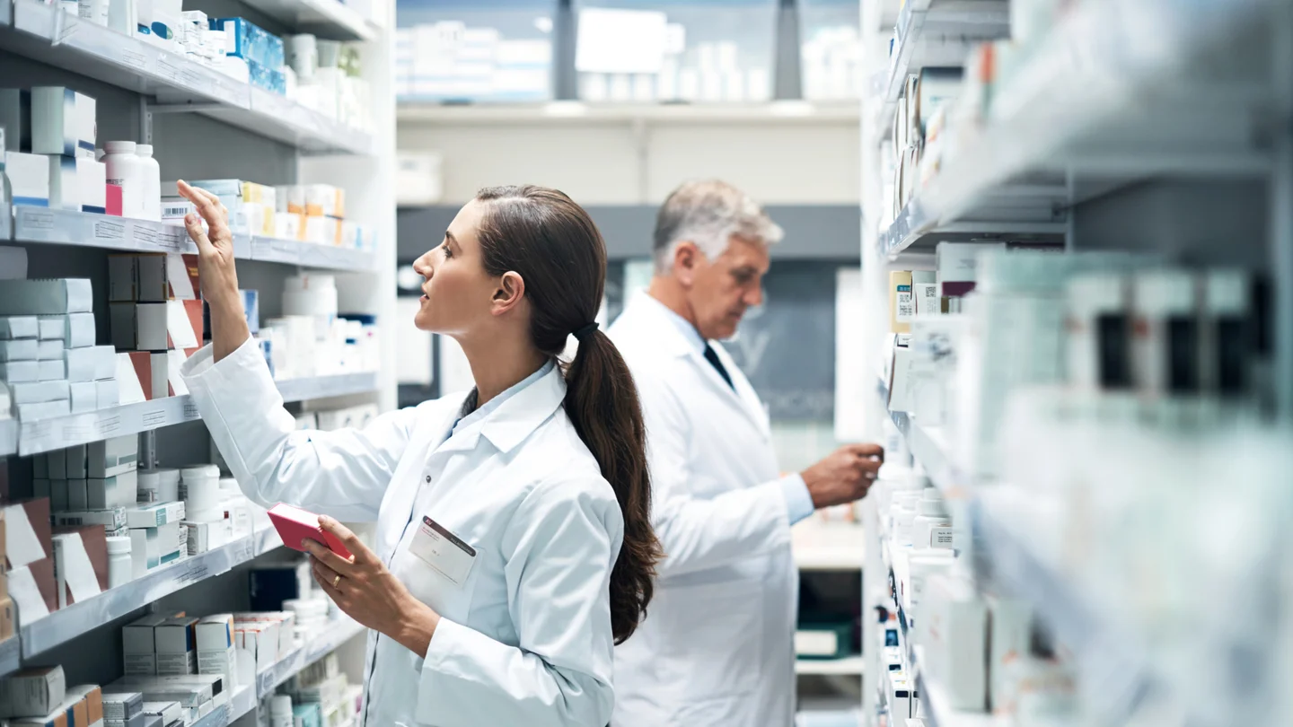 Apothekerin und Apotheker sortieren Medikamente in Regale ein. 