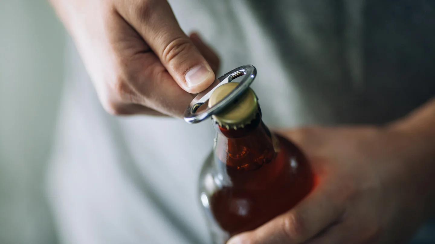 Eine Bierflasche wird mit einem Flaschen&ouml;ffner ge&ouml;ffnet.