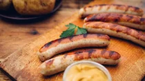 Erhöhte Cholesterinwerte: Auf einem Holzbrett liegen frisch gegrillte Bratwürste.