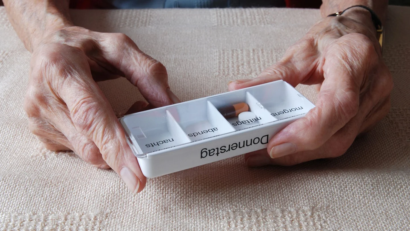 Eine &auml;ltere Frau h&auml;lt eine Tablettenbox in den H&auml;nden. 
