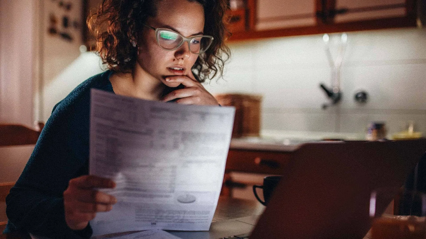 Eine Frau sitzt vor einem Laptop und h&auml;lt ein Informationsblatt in der Hand.