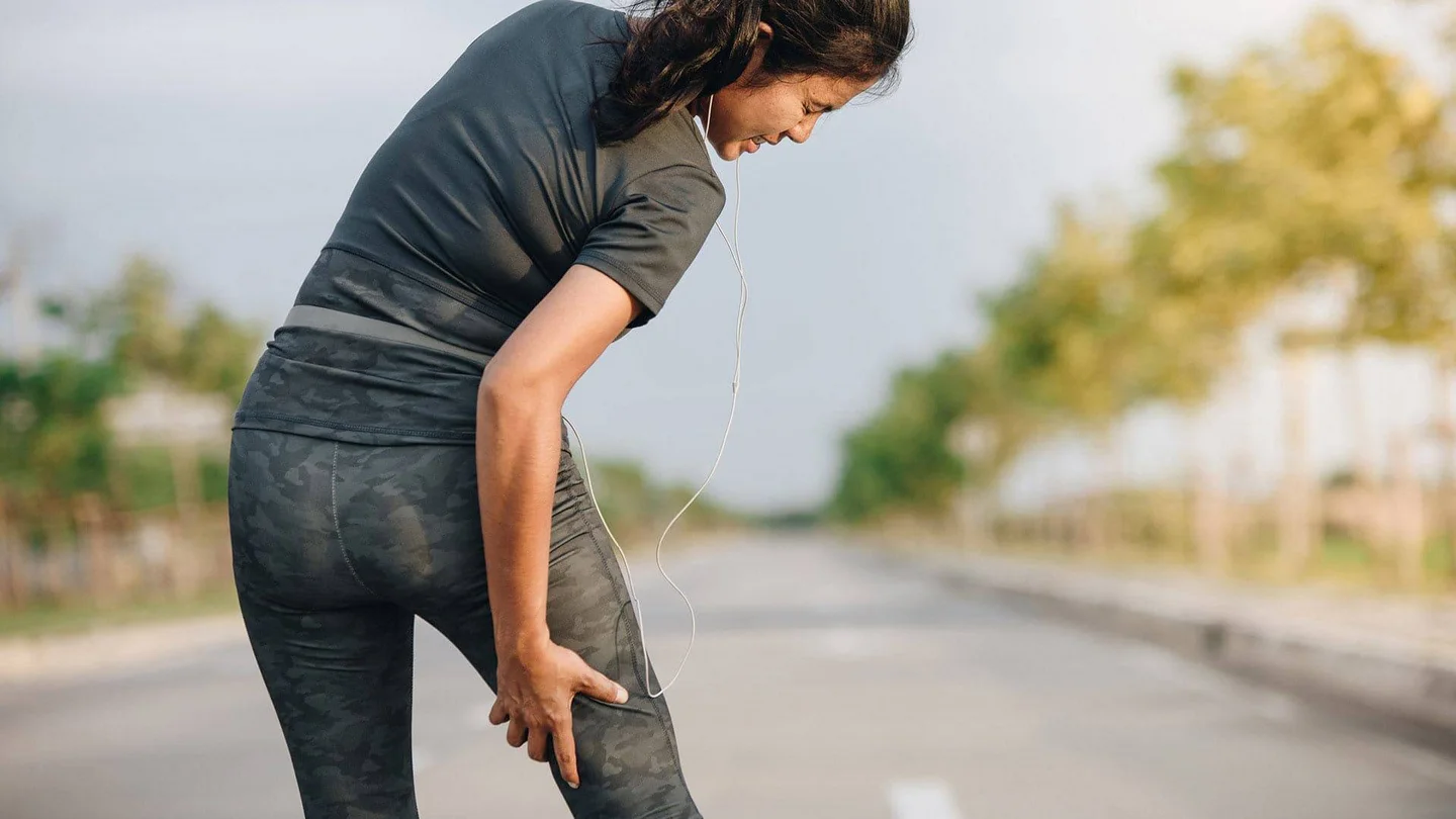 Eine Joggerin greift sich an den schmerzenden hinteren Oberschenkel.