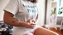 Ovarialzysten: Eine Frau sitzt auf einem Bett und hält sich mit beiden Händen den Bauch.