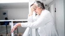 Eine ältere Frau fasst sich mit einer Hand an die Stirn.