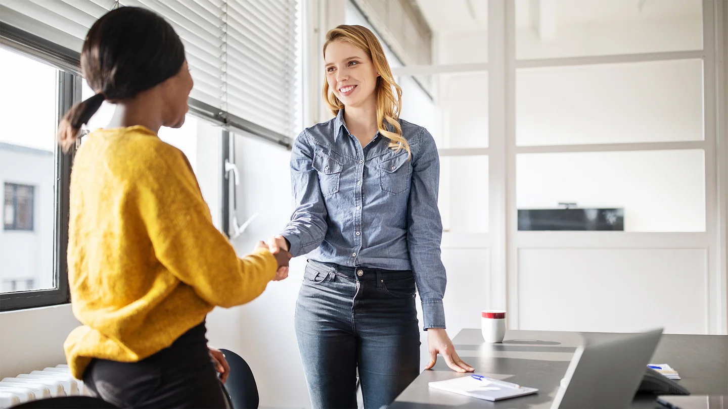 Betriebliches Eingliederungsmanagement: Zwei Frauen stehen an einem B&uuml;rotisch und sch&uuml;tteln sich nach einem erfolgreichen gesch&auml;ftlichen Gespr&auml;ch zustimmend die H&auml;nde.